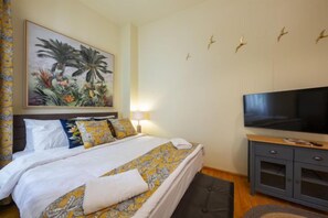 A hotel room with a bed, a television, a painting, and a wall-mounted light fixture. - Rainforest Studio Downtown by Pretty Apartments (Bucharest)