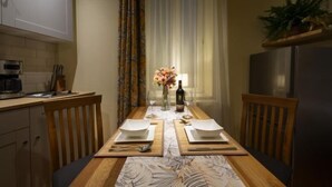 A dining area with a wooden table set for two, a vase with flowers, and a bottle of wine on the table. - Rainforest Studio Downtown by Pretty Apartments (Bucharest)