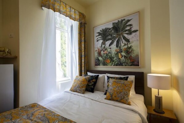A hotel room with a bed, a nightstand with a lamp, a painting on the wall, and a window with curtains. - Rainforest Studio Downtown by Pretty Apartments (Bucharest)