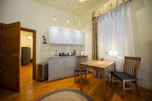 A compact kitchen with white cabinets, a dining table with chairs, and a window with curtains. - Rainforest Studio Downtown by Pretty Apartments (Bucharest)