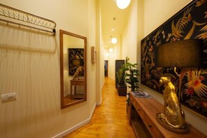 A hallway with a wooden bench, a mirror, a decorative lamp, and a wall with a floral pattern. - Rainforest Studio Downtown by Pretty Apartments (Bucharest)
