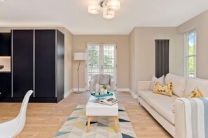 Un salon avec un canapé, une table basse, un fauteuil, une lampe et une vue par la fenêtre.