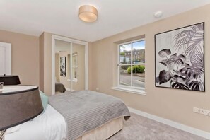 A bedroom with a bed, a bedside table, a window, and a door. - Modern central 2 bedroom apartment with parking (Edinburgh)