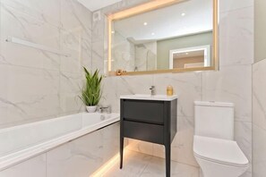 A bathroom with a bathtub, a sink, a toilet, and a mirror. - Modern central 2 bedroom apartment with parking (Edinburgh)