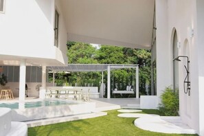 Ein modernes Haus mit Pool, Terrasse und überdachter Sitzgelegenheit.