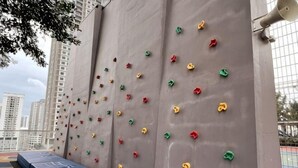A climbing wall with various colored holds, a blue padded area at the bottom, and a metal structure to the right. - Georgetown Urban Suite Family Skypool I SeaView (Jelutong)