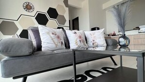 A modern living room with a grey sofa, decorative pillows, a black coffee table, and a hexagonal wall design. - Georgetown Urban Suite Family Skypool I SeaView (Jelutong)