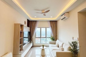 Un soggiorno moderno con un ventilatore a soffitto, una TV a schermo piatto, un divano, un tavolino da caffè e un'ampia finestra con tende.