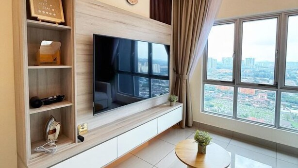A modern living room with a large flat-screen TV mounted on a wooden wall, a built-in shelf with various items, a round coffee table, and a large window offering a city view. - Nexus Kajang by Luvit Stay (Kajang)