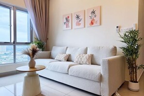 A living room with a sofa, a small table, and a potted plant. There are three framed pictures on the wall.