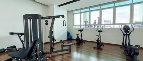 A gym with exercise equipment, large windows, and a wooden floor.