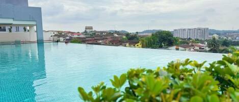 An infinity pool with a view of distant buildings and a cloudy sky.