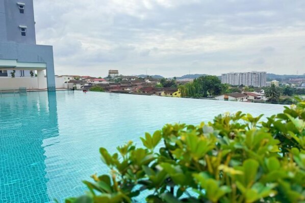 An infinity pool with a view of distant buildings and a cloudy sky.