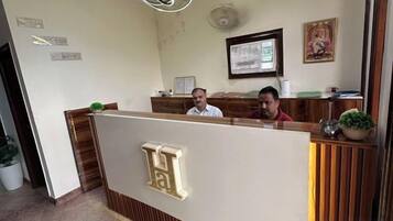 A reception desk with a logo, a seated receptionist, and a framed document on the wall.