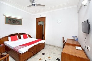 A bedroom with a bed, a desk, a chair, a television, a ceiling fan, and a door. - HOTEL ASHISH (Baddi)