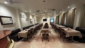 Un restaurante amplio con varias mesas y cabinas, un televisor de pantalla plana en la pared y un ventanal con cortinas.
