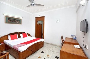 Un dormitorio con cama, escritorio, silla, ventilador de techo, televisor y una puerta.