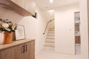 A hallway with a wooden cabinet, a framed picture, and a staircase leading to another room. - Tsubakirakukyo (Osaka)