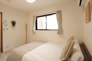 A bedroom with a single bed, a window with curtains, a wall-mounted plant, and a coat rack. - Tsubakirakukyo (Osaka)