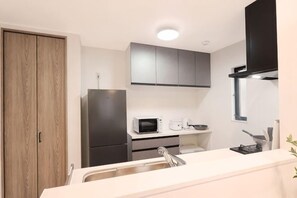 A modern kitchen with a built-in microwave, stainless steel sink, and black cabinets. - Tsubakirakukyo (Osaka)