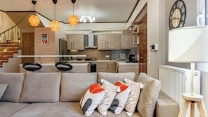 Una sala de estar moderna con sofá, cojines decorativos, luces colgantes y vistas a la cocina y la escalera.