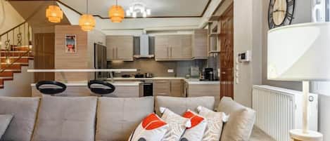 Ein modernes Wohnzimmer mit einer Couch, Pendelleuchten und Blick auf eine Küche und eine Treppe.