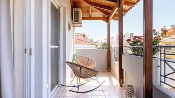 A balcony with a wooden ceiling, a sliding glass door, a wicker chair, and a small table.