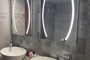 Ein modernes Badezimmer mit großem Spiegel, zwei Waschbecken und einer Duschkabine.