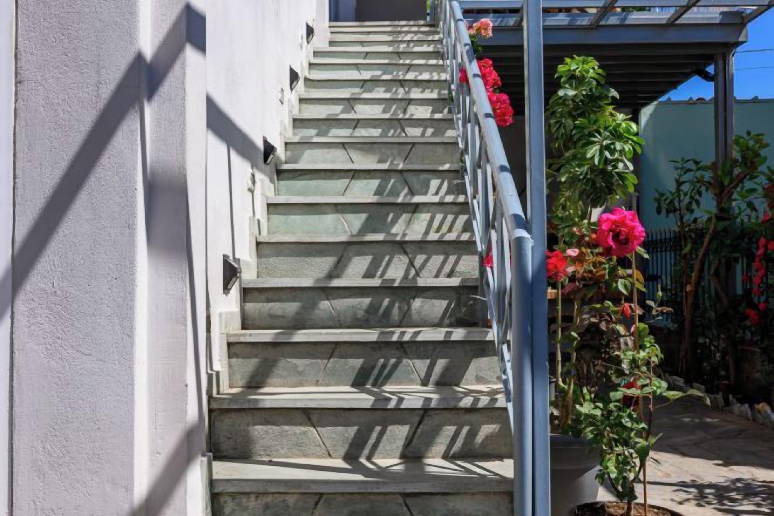 A staircase with metal railings, leading to a covered area with potted plants and flowers.