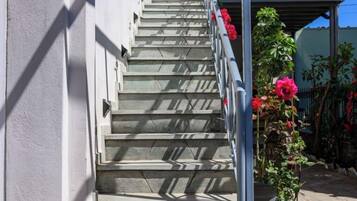 A staircase with metal railings, leading to a covered area with potted plants and flowers.