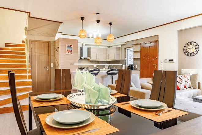 A dining area with a table set for four, a staircase, and a kitchen in the background.