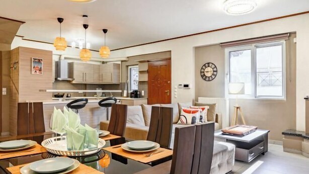 Un comedor moderno con una mesa de madera dispuesta para cuatro, una cocina al fondo y un ventanal con vistas.