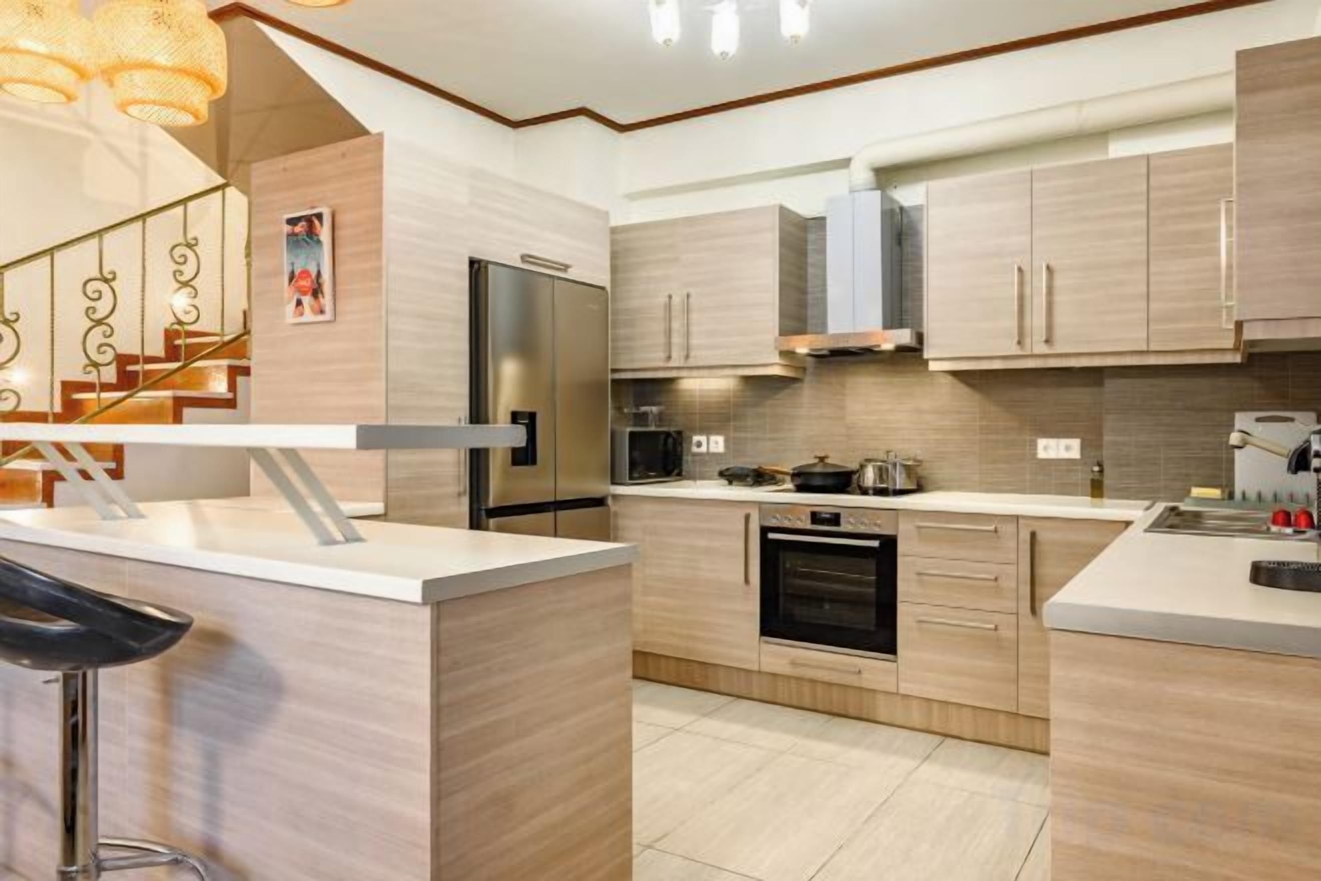 A modern kitchen with a central island, stainless steel appliances, and light wood cabinetry.