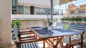 Un patio al aire libre con una mesa y sillas de madera, una planta en maceta y vistas a un edificio con balcones.