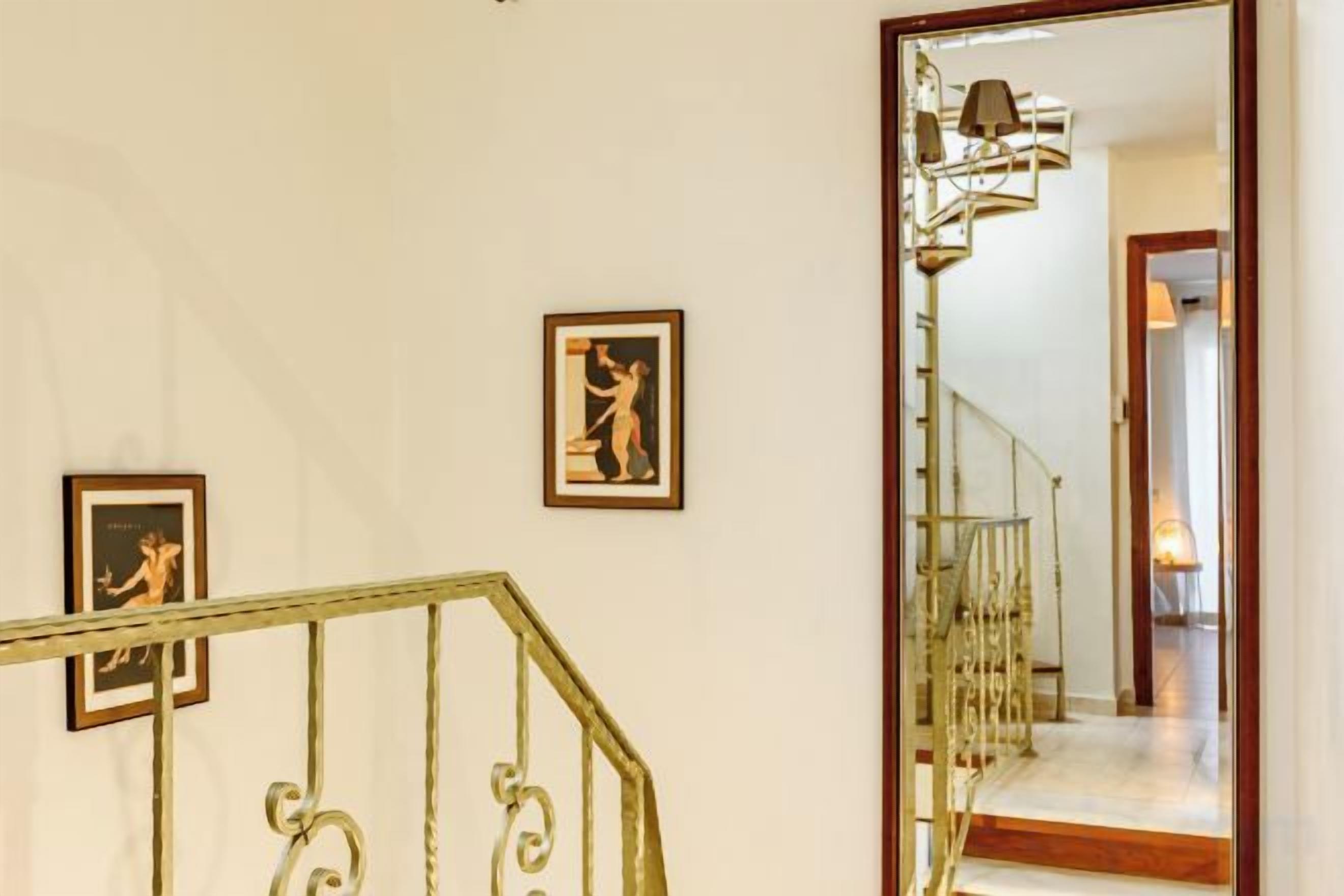 Un escalier avec une rampe en métal, un mur orné de tableaux encadrés et un miroir qui reflète un couloir.