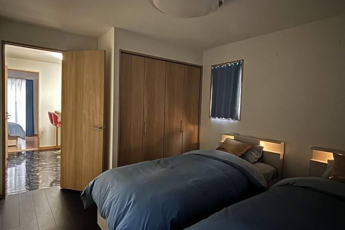 A bedroom with two beds, a wardrobe, a mirror, and a window with curtains.