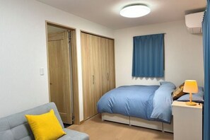 A bedroom with a bed, a nightstand, a lamp, a wardrobe, and a sofa with a pillow. - Lapis House 201-3F (Tokyo)