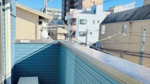 Un balcon étroit avec un banc, donnant sur une zone urbaine densément peuplée, où se trouvent différents bâtiments.