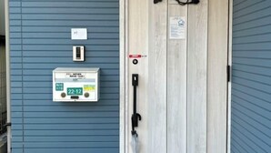 Une entrée d’immeuble avec un mur extérieur bleu, une porte en bois dotée d’une poignée noire et une boîte de raccordement portant l’étiquette « 22-12 ».