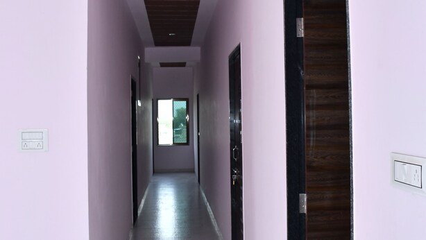 Un pasillo con paredes rosas, una puerta de madera y techo con detalle rojo.