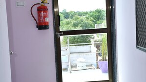 Una puerta con un extintor colgado en la pared, vistas de vegetación al exterior y suelo de baldosas.