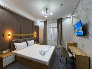 A hotel room with a bed, bedside tables, a desk, a chair, a television, and a ceiling light fixture. - Marco Polo (Tashkent)