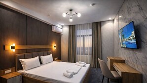 A hotel room with a bed, bedside tables, a desk, a chair, a TV, and a window with curtains. - Marco Polo (Tashkent)