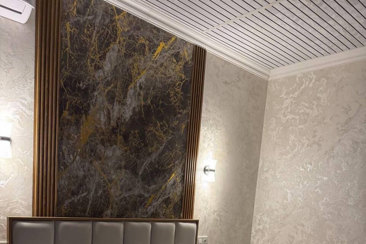 A hotel room with a large bed, a marble accent wall, and a modern ceiling design.