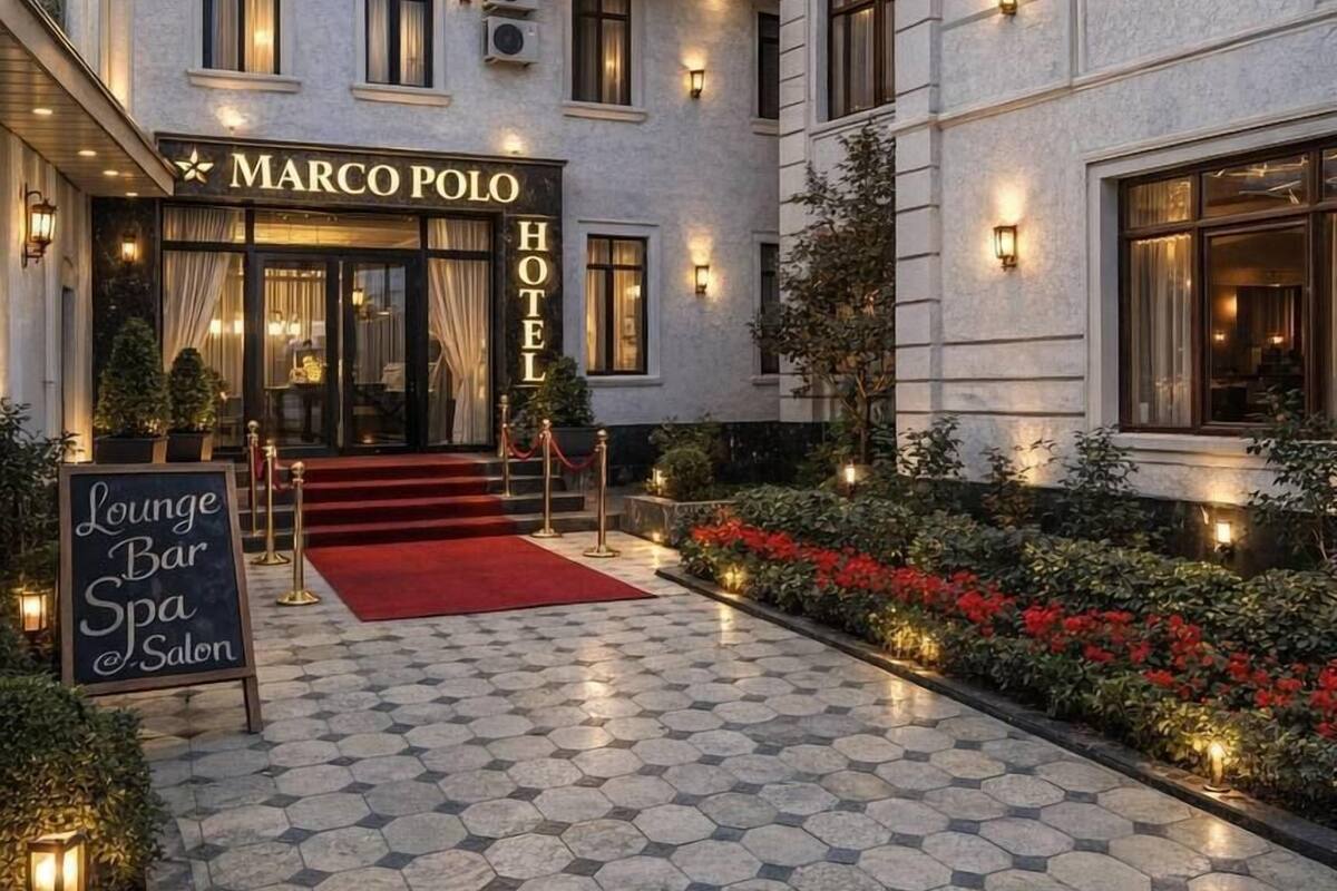A hotel entrance with a sign reading 'Marco Polo Hotel,' a red carpet, and a hexagonal tiled courtyard.