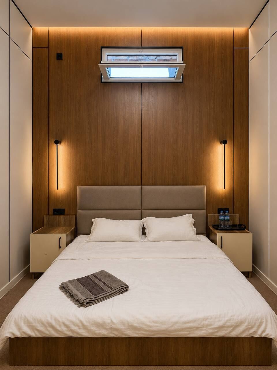 A hotel room with a large bed, wooden panel walls, a ceiling-mounted air conditioning unit, and bedside lamps.