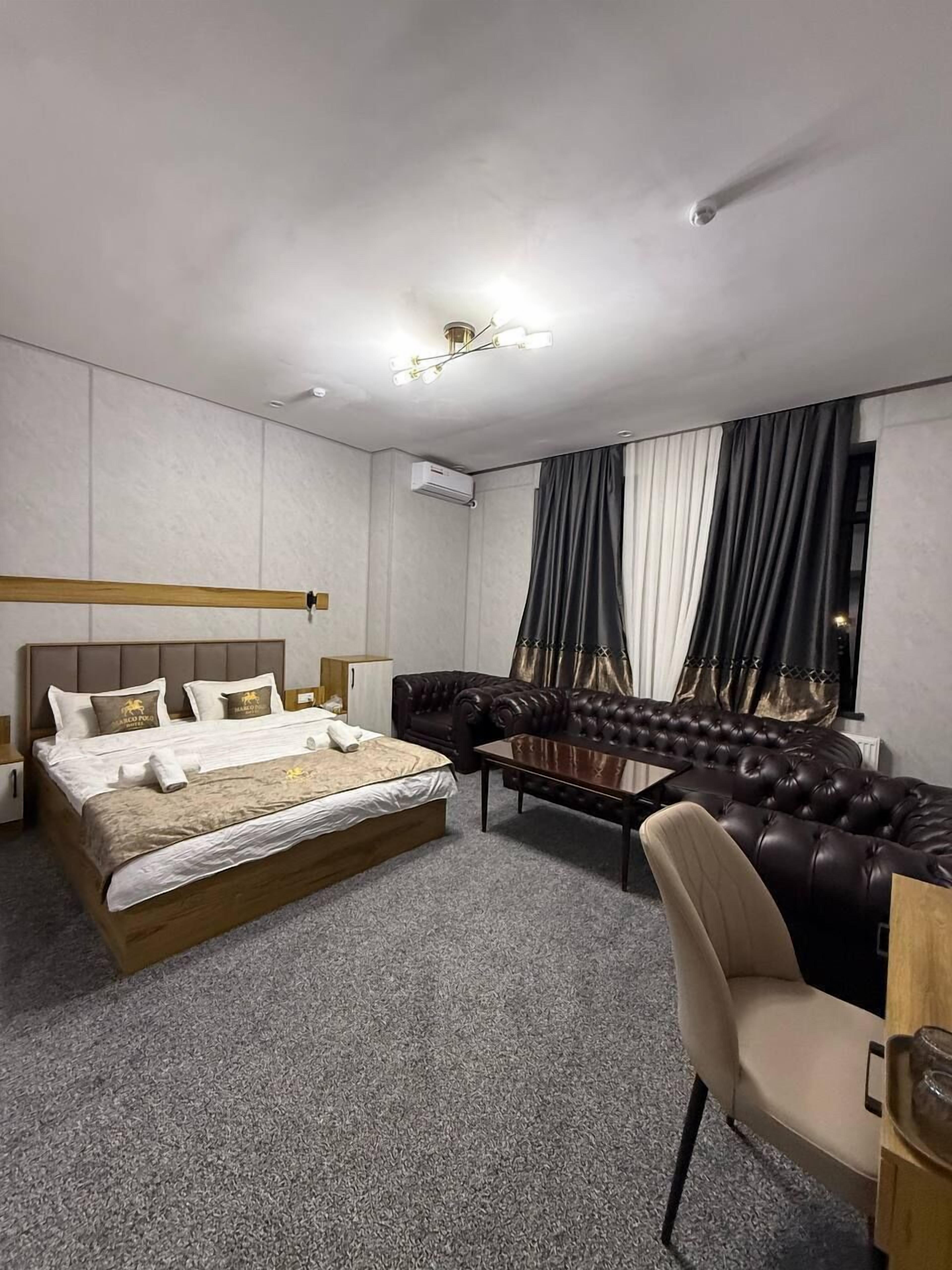 Ein Hotelzimmer mit einem Bett, einem Sofa, einem Sessel, einem kleinen Tisch und einem Fenster mit Vorhängen.