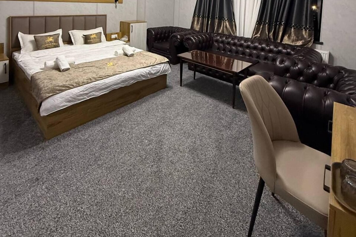 A hotel room with a bed, a sofa, a chair, a small table, and a window with curtains.