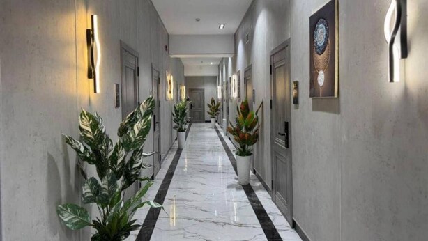 A hallway with marble flooring, potted plants, wall-mounted light fixtures, and a door with a decorative plate. - Marco Polo (Tashkent)