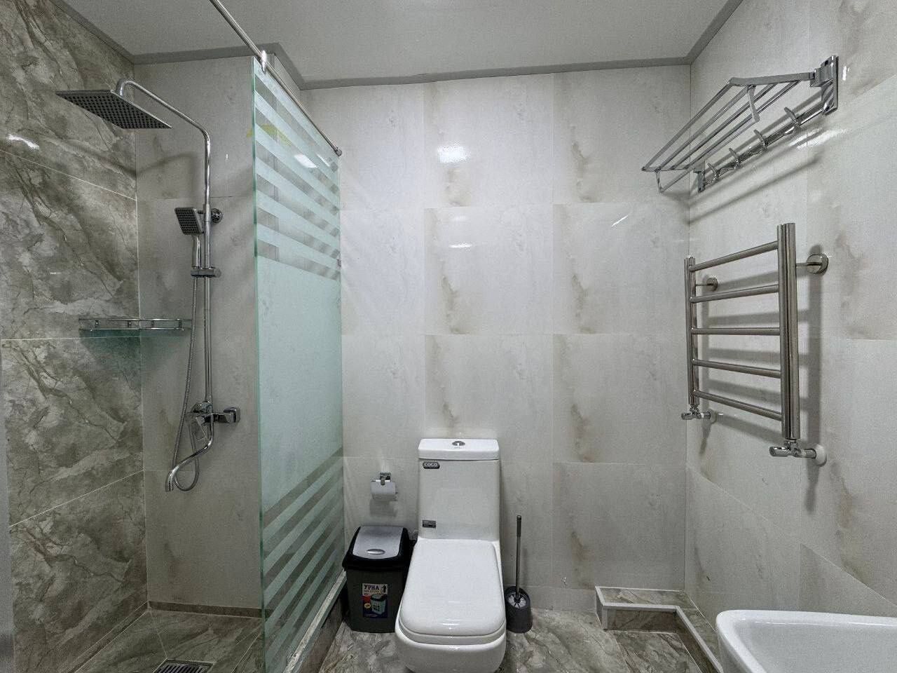 A bathroom with a glass-enclosed shower, a toilet, a bathtub, and a towel rack.